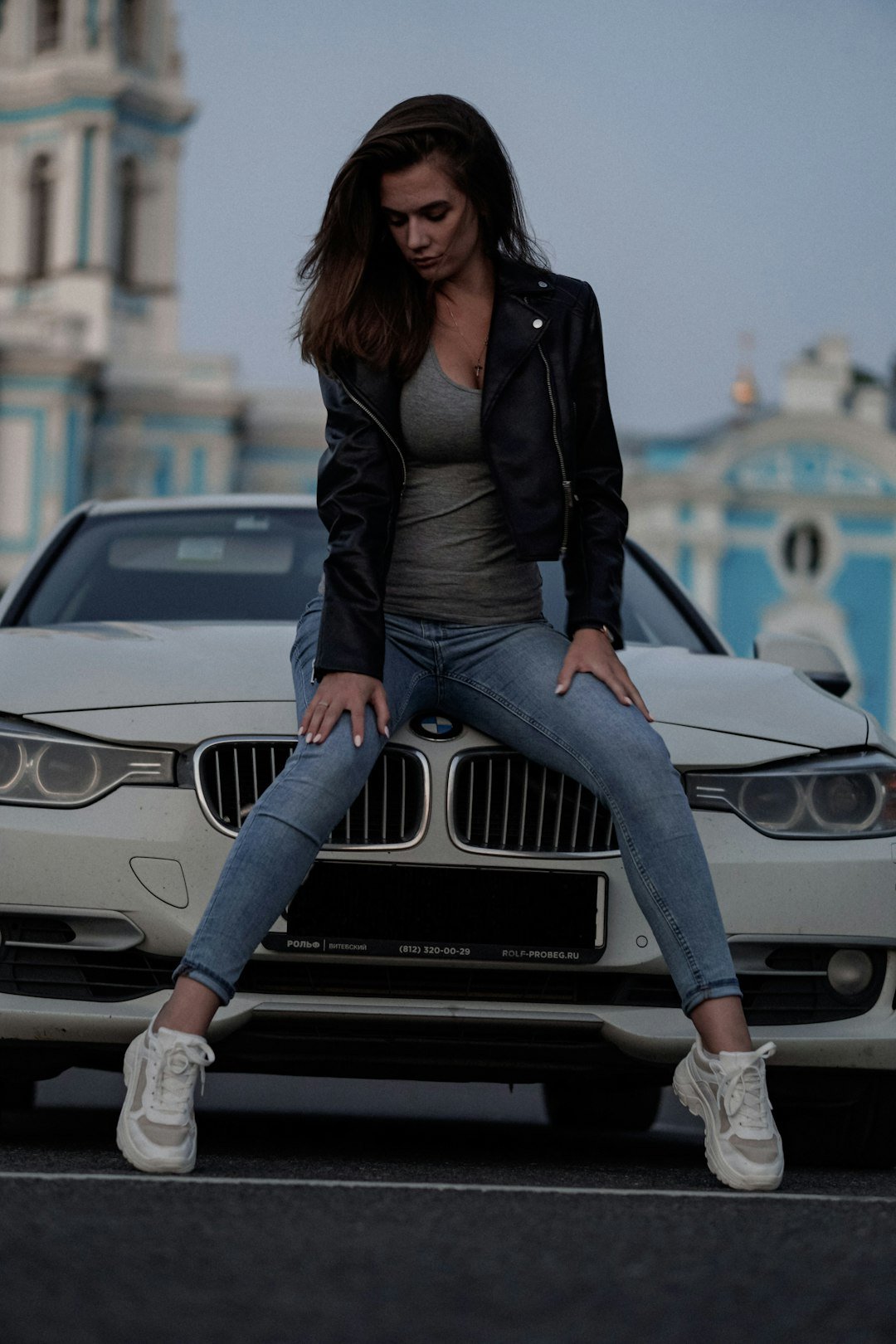 woman in black leather jacket and blue denim jeans sitting on white mercedes benz car