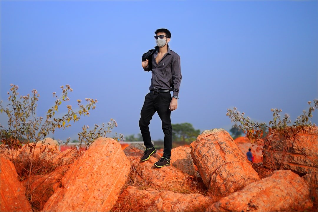 man in gray jacket and black pants standing on brown rock during daytime