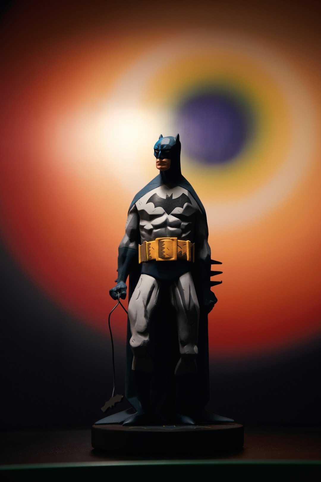 Batman stands ready in front of a colorful backdrop.