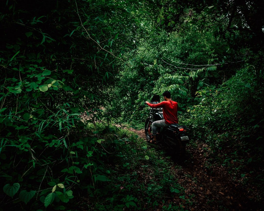 man in red jacket sitting on black motorcycle surrounded by green plants during daytime